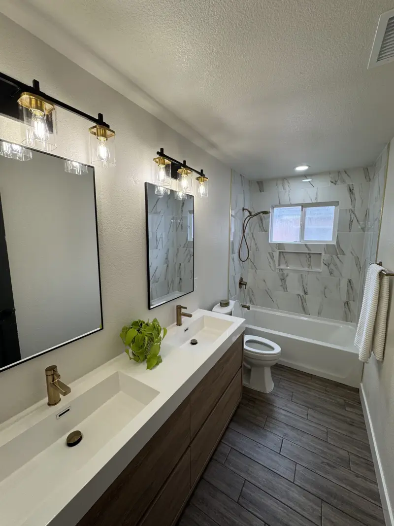 Bathroom with marble-look tub surround, long white vanity and brass faucet