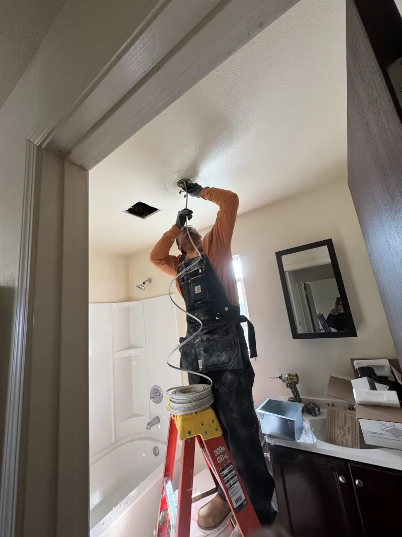 JKC crew member installing a ceiling fixture in a bathroom