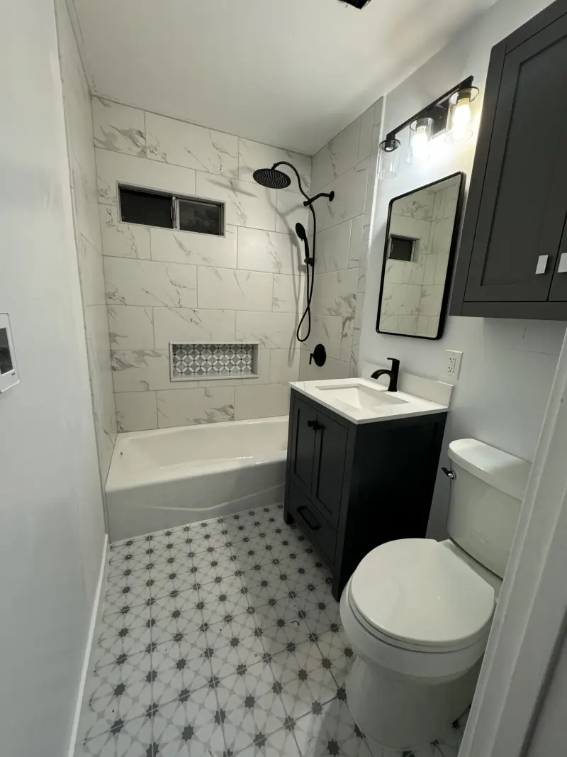 Bathroom remodel with marble-look tile, a recessed shower niche, black fixtures and a dark vanity