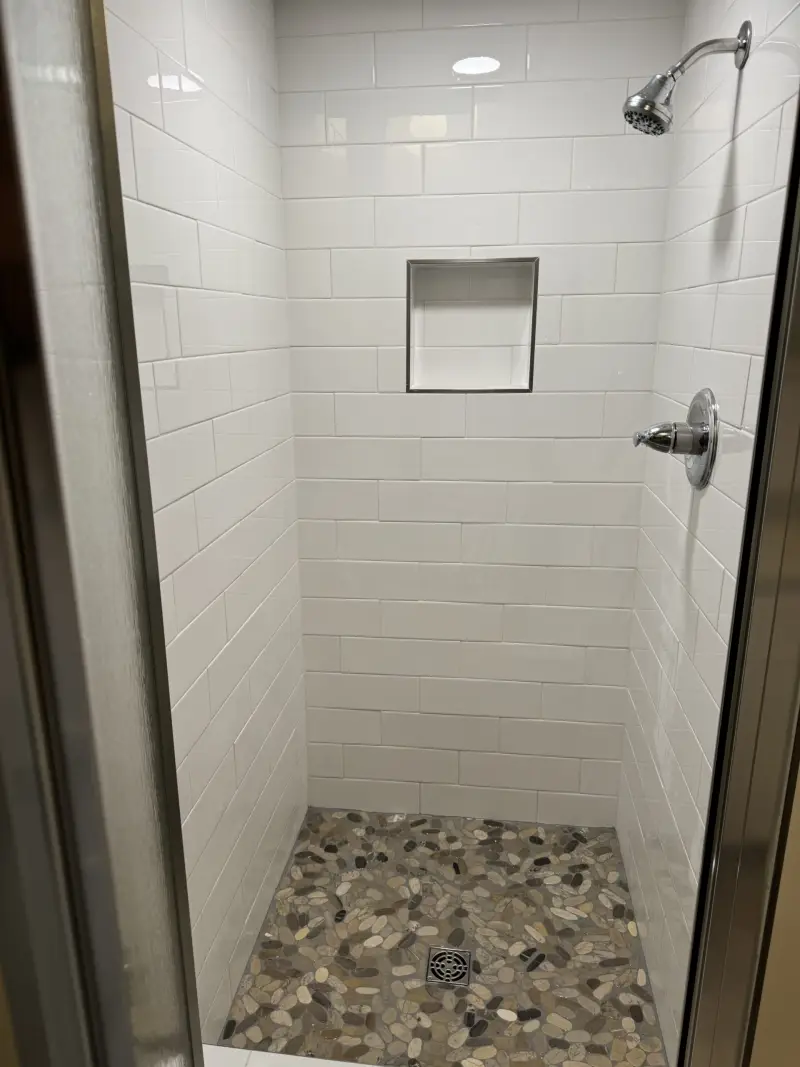 Walk-in shower with white tile walls, a recessed niche and a pebble floor