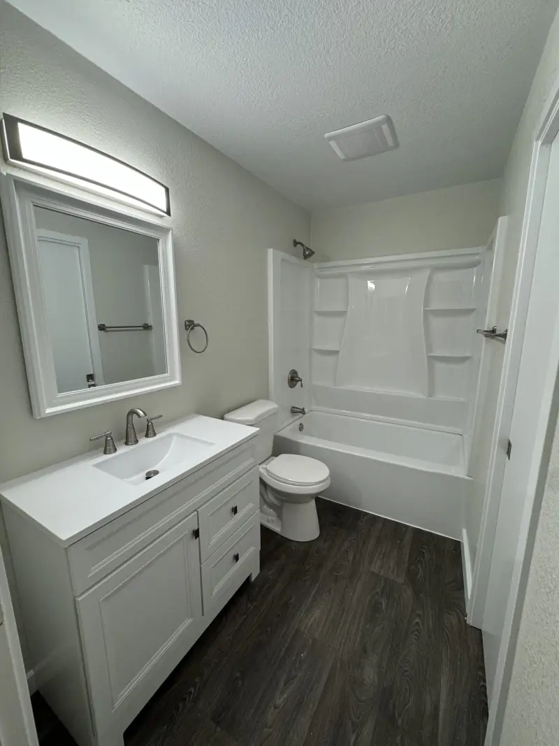Bathroom with a new white vanity, tub and shower surround and wood-look vinyl flooring