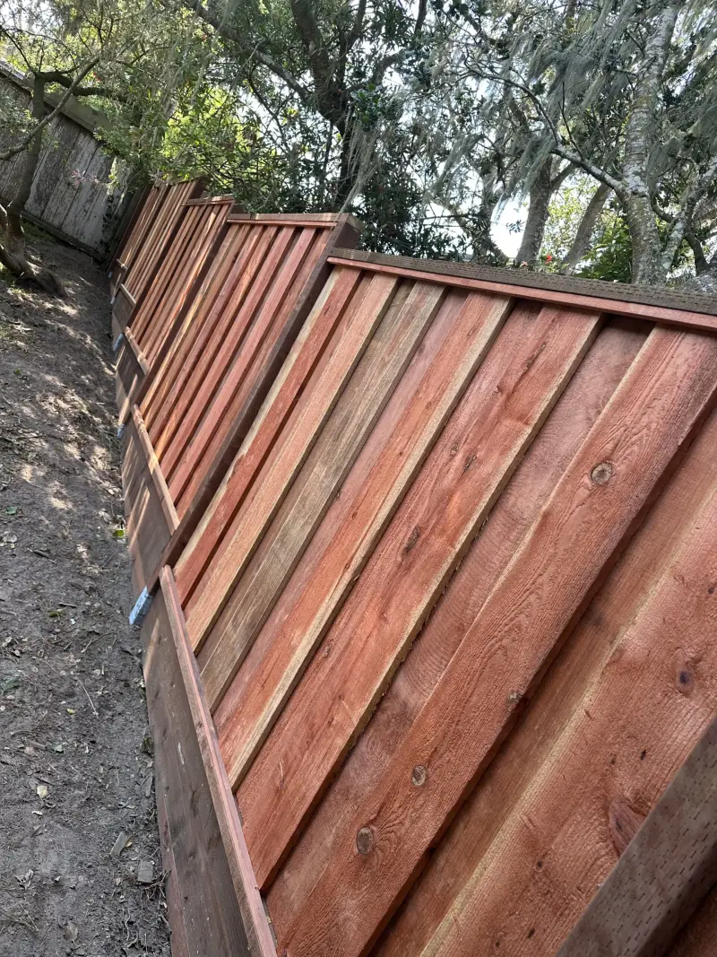 Stained redwood privacy fence with a cap rail following a sloped yard