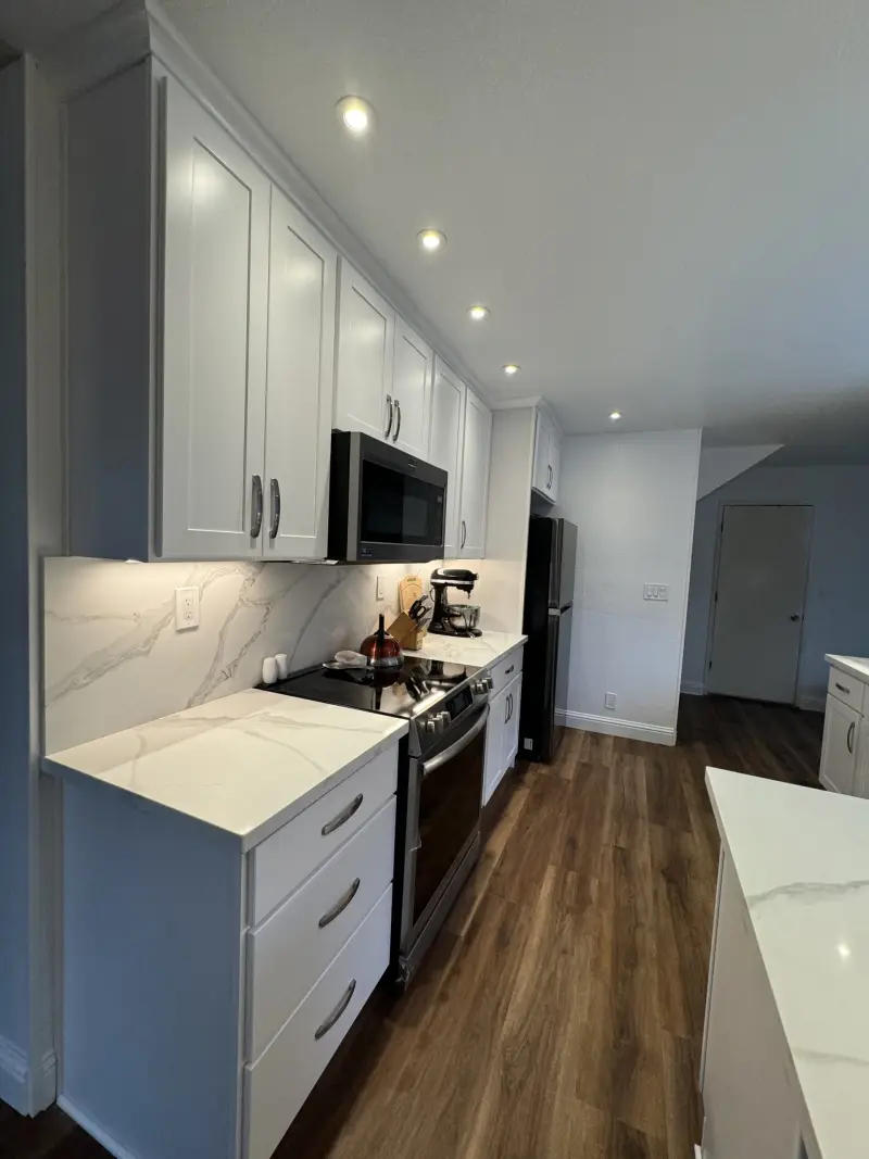 Galley kitchen with white cabinets, quartz countertops and under-cabinet lighting
