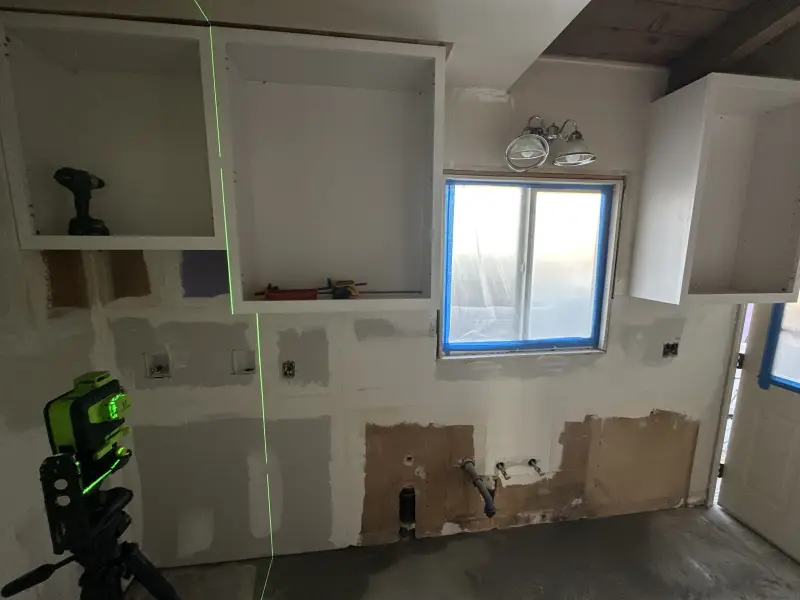 Kitchen wall opened up and patched for new cabinets and plumbing, laid out with a laser level