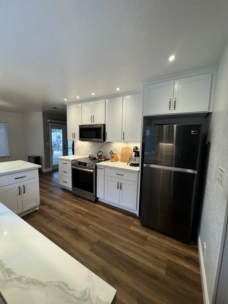 Remodeled kitchen with white shaker cabinets, stainless steel appliances and wood-look flooring